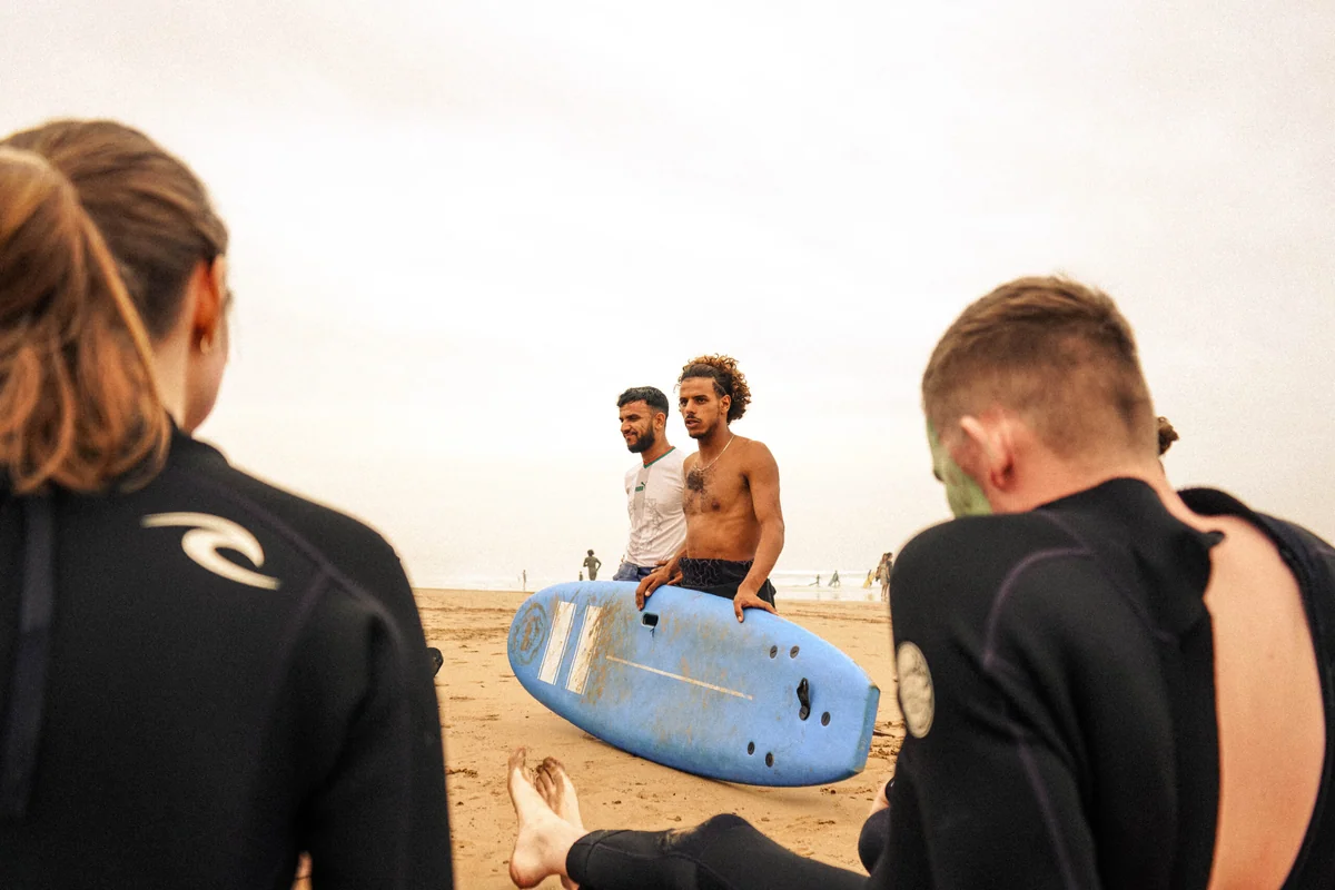 Surf instructor coaching a beginner on a foam surfboard at a Moroccan beach break